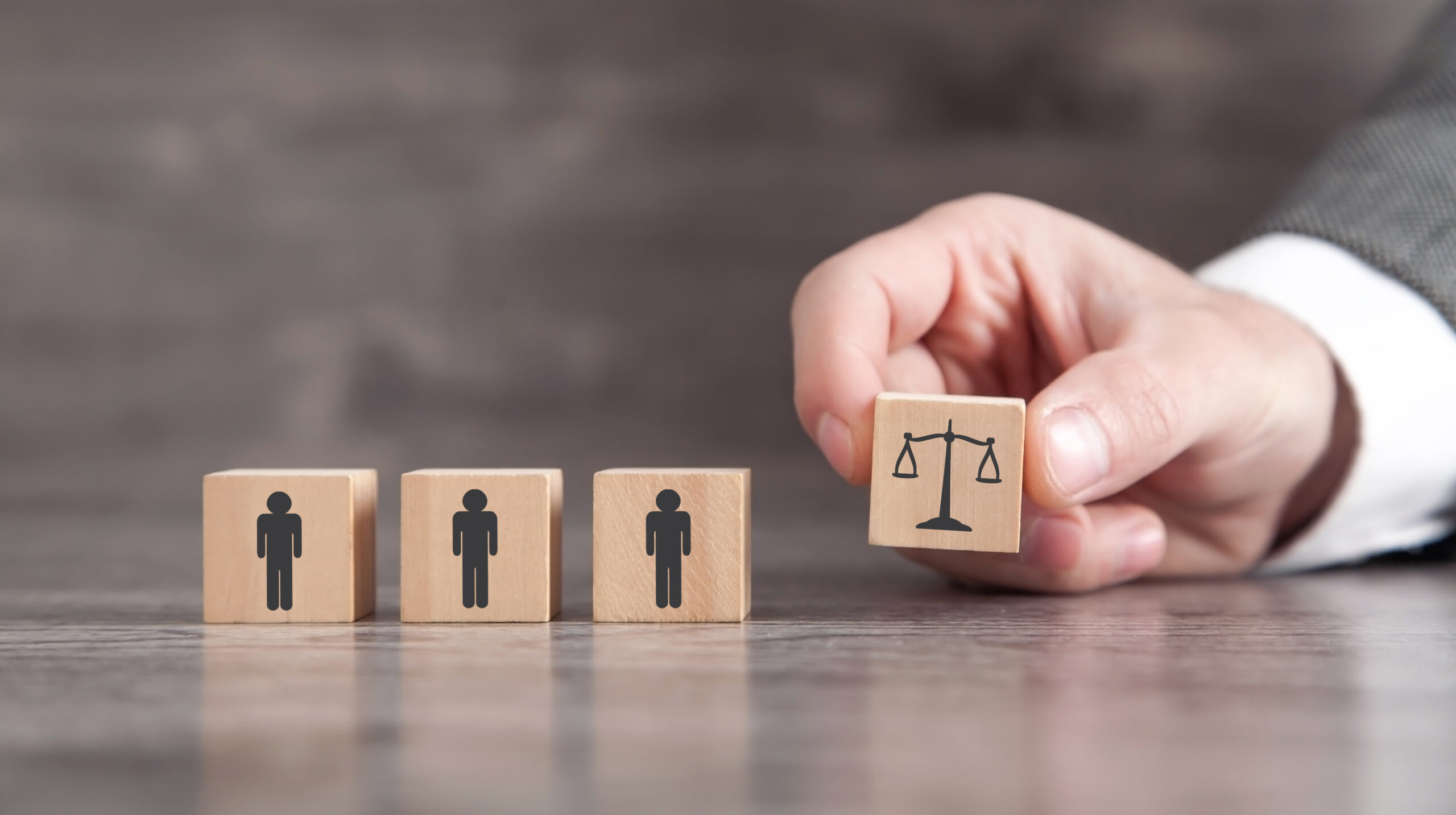 Male hand showing judge scales and human icons on wooden cubes.